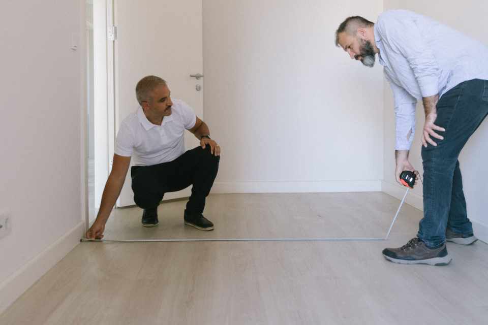 two men measuring the width of a room to calculate square footage
